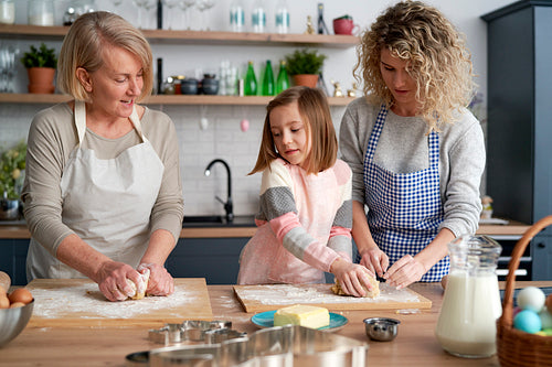 Three generations of women kneading dough in kitchen.