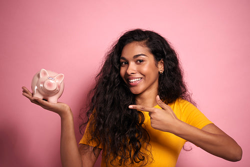 Smiling African woman pointing the piggy bank in studio shot.