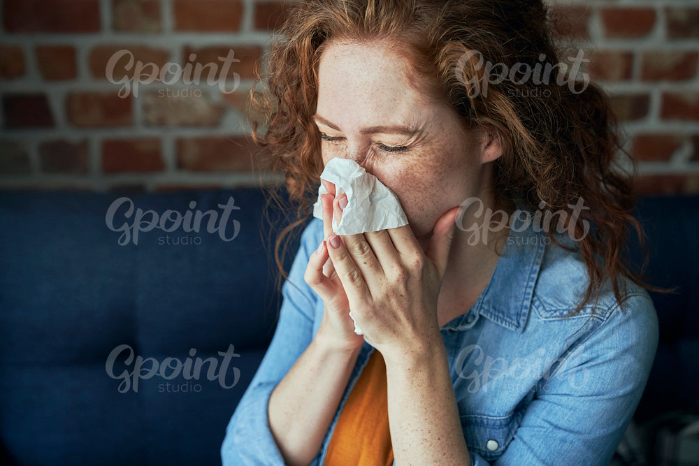 Young caucasian  red head woman blowing nose into tissue at home 