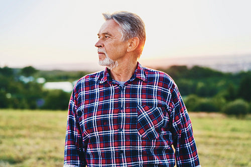 Senior man looks over his land at sunset