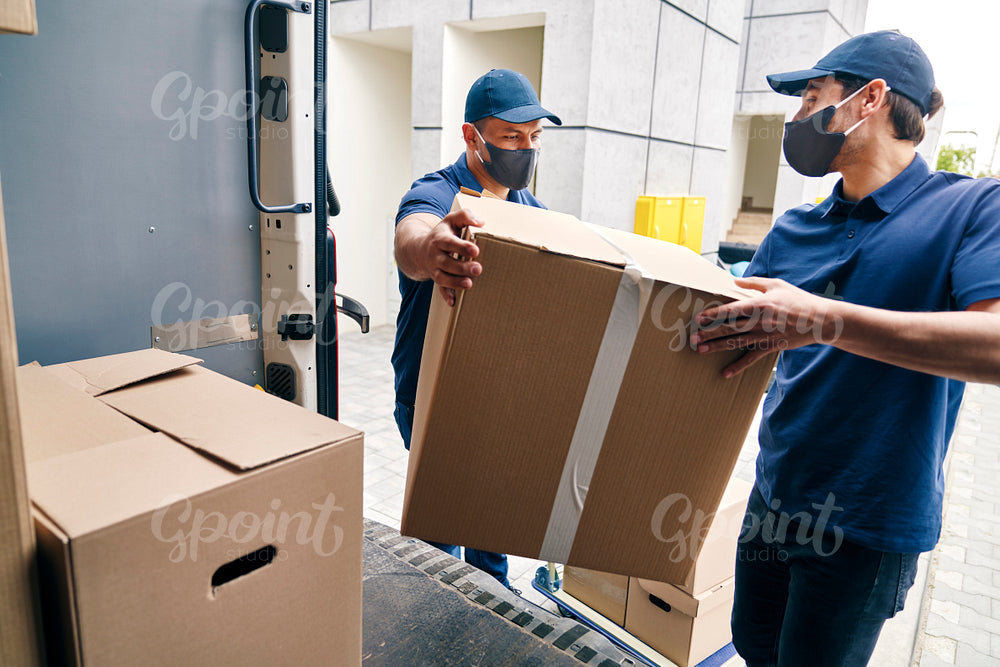 Couriers in protective masks unloading packages from a delivery truck