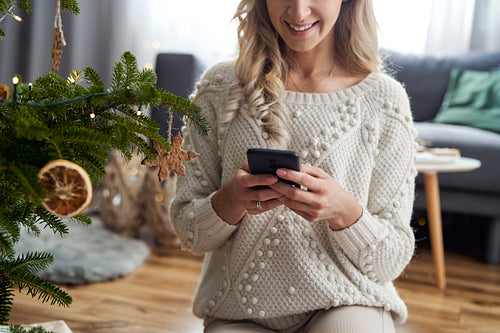 Unrecognizable caucasian woman using phone sitting next to Christmas tree