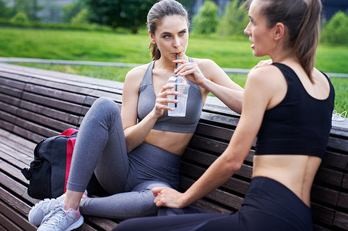 Women in training clothes drinking an isotonic drink outdoors
