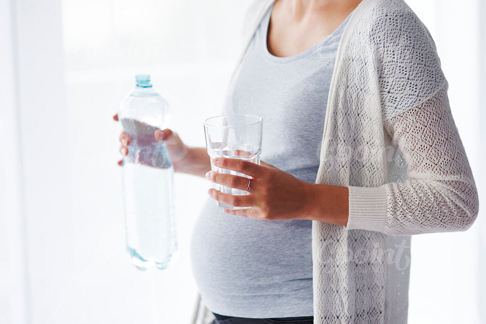 Unrecognizable pregnant woman drinking water