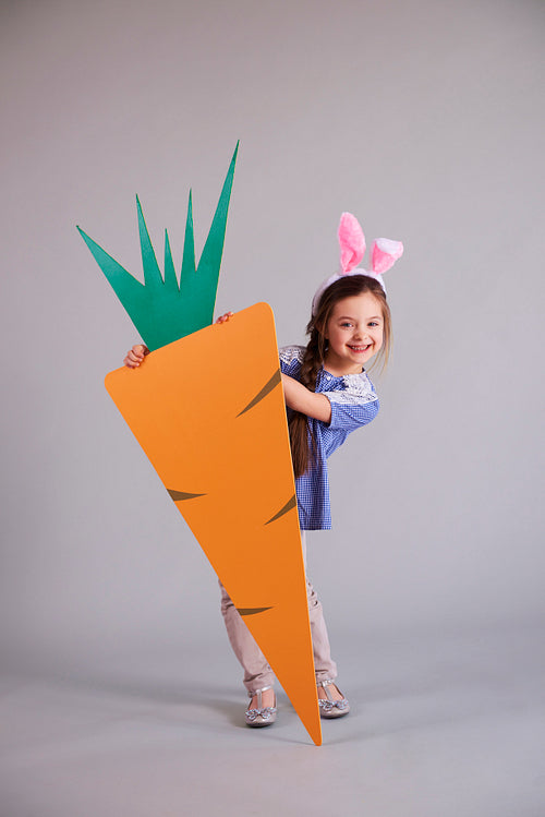 Adorable girl with bunny ears holding a big carrot