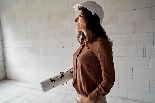 Female mature caucasian engineer standing on construction site and browsing building plans