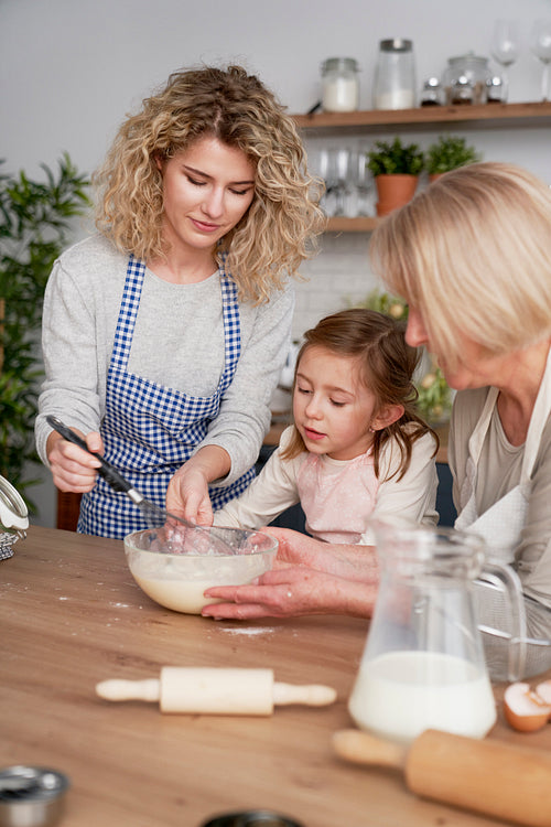 Three generations of women mixing ingredients in a bowl
