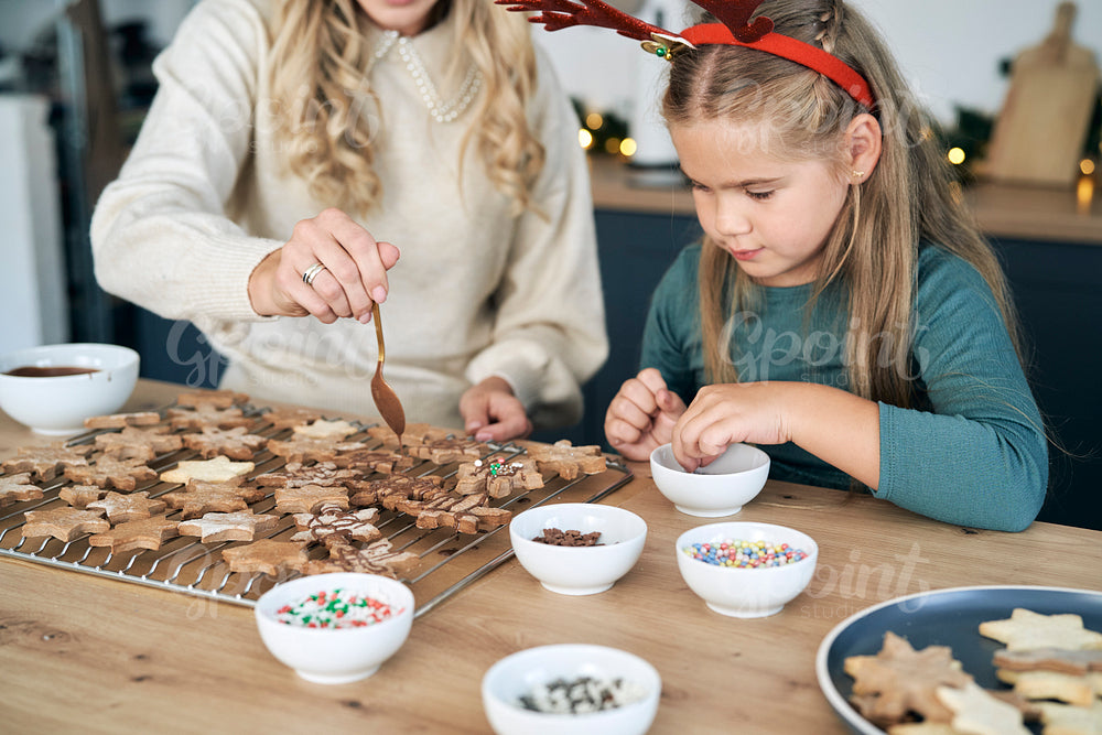 Caucasian mother and daughter decorating gingerbread cookies on Christmas time