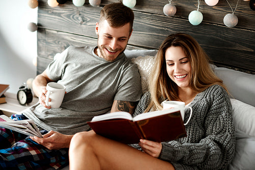 Happy young couple with coffee reading in bed