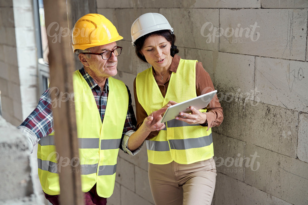 Two caucasian engineers standing on stairs and discussing over digital tablet on the construction site