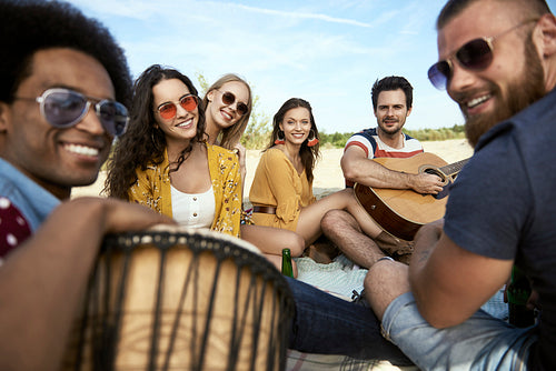 Portrait of happy friends sitting on beach with musical instruments