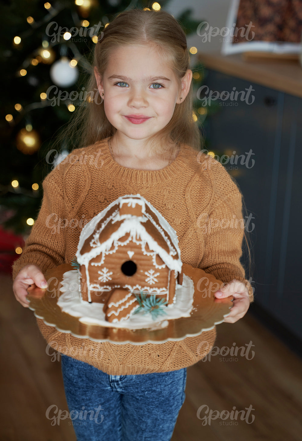 Little girl holding decorated gingerbread house