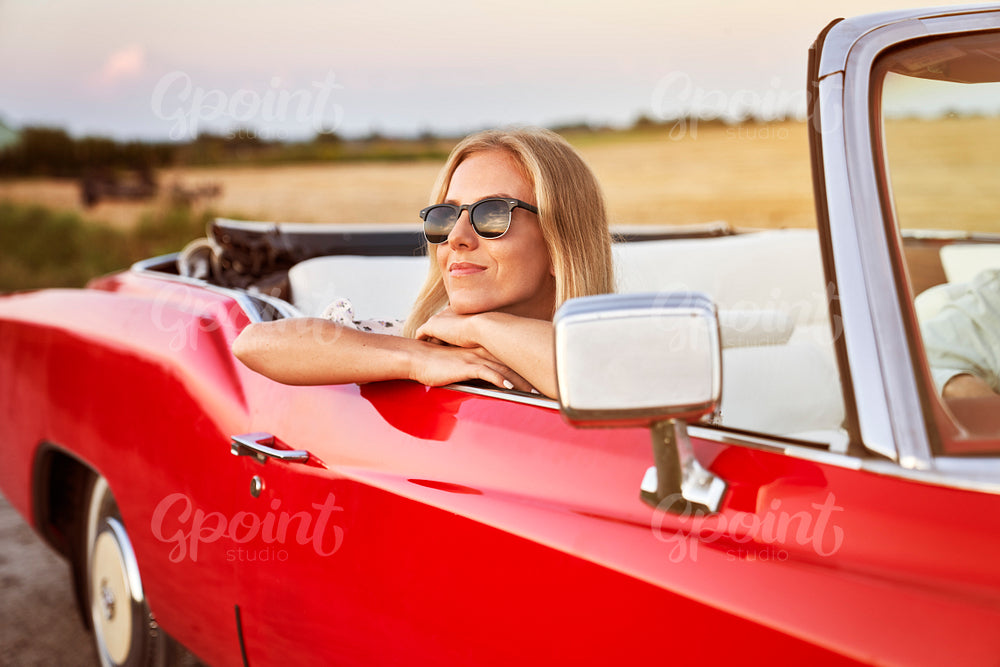 Beautiful woman sitting in car at sunset