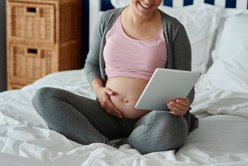 Unrecognizable pregnant woman using tablet in bed