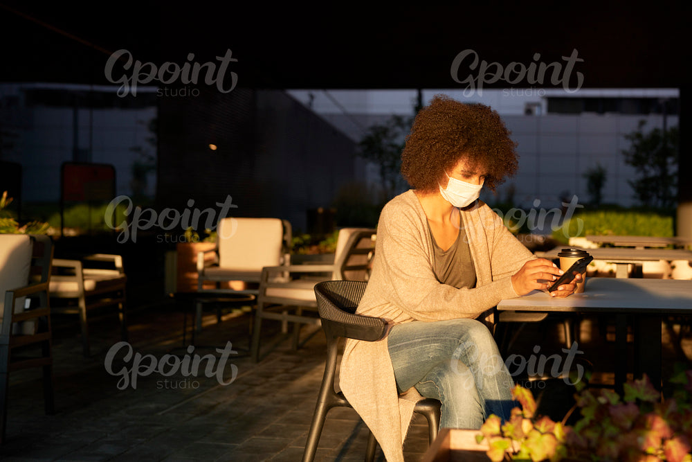 Woman in face mask sitting in a cafe outdoors